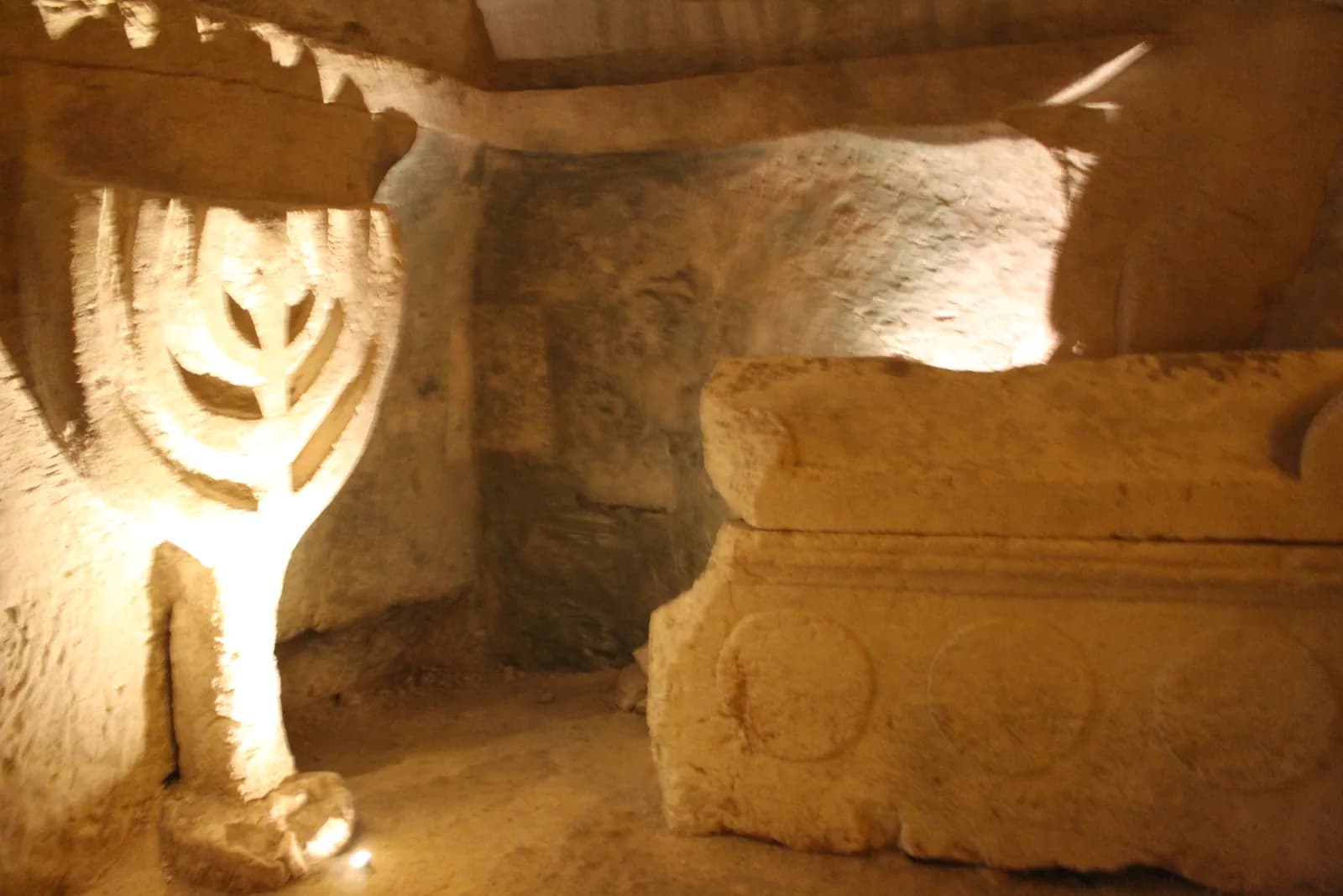 תבליט המנורה החצוב בקיר ולידו ארון קבורה מעוטר במערת הארונות
