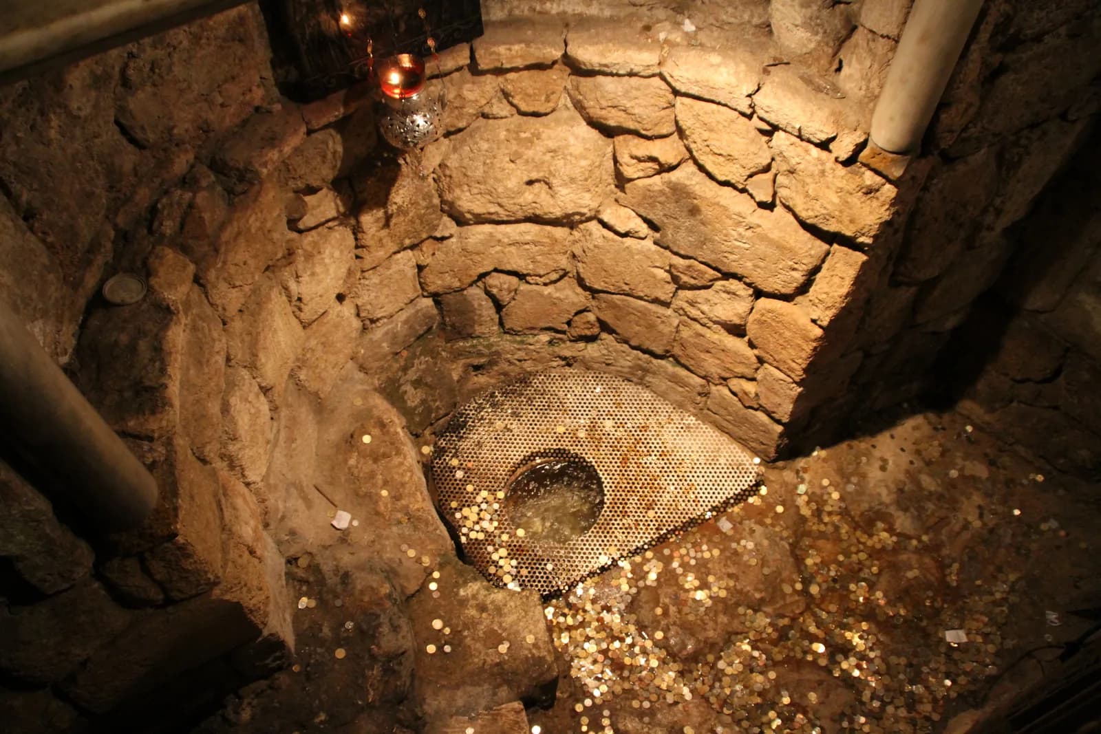 פתח המעיין בקצה הקריפטה, ובתוכו מטבעות שהשליכו מבקרים