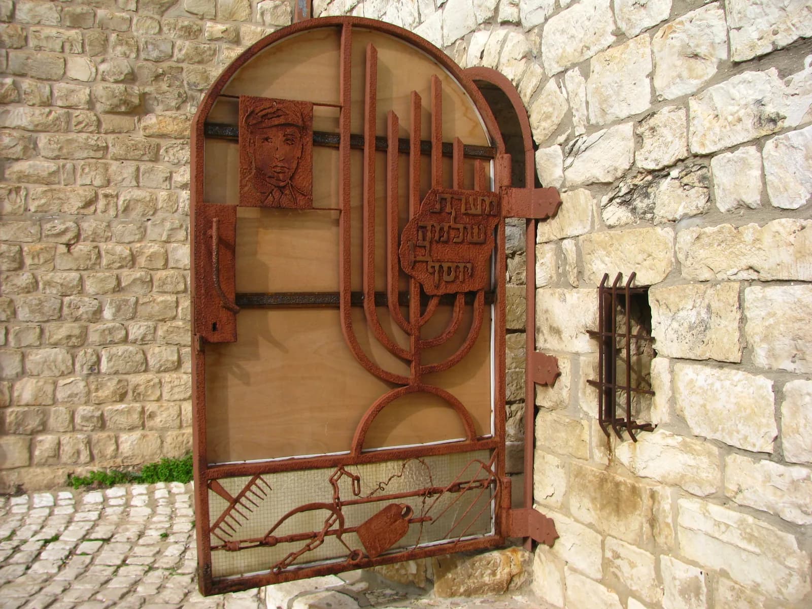 דלת הכניסה למערת שלמה בן יוסף פתוחה, בקיר האבן של המושבה הוותיקה בראש פינה