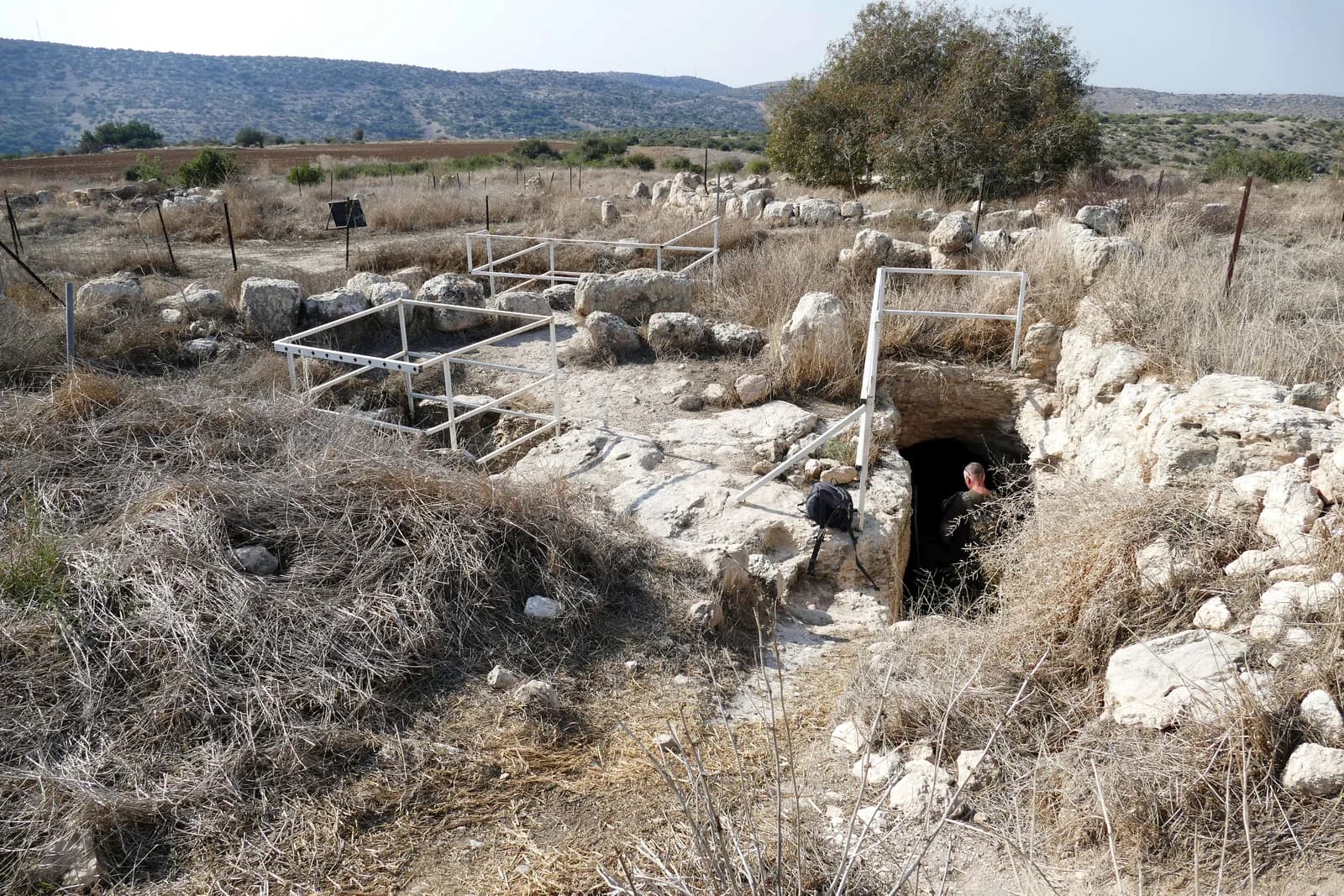 פתח כניסה למערה תת-קרקעית בין שרידי החורבה, וברקע נוף השפלה