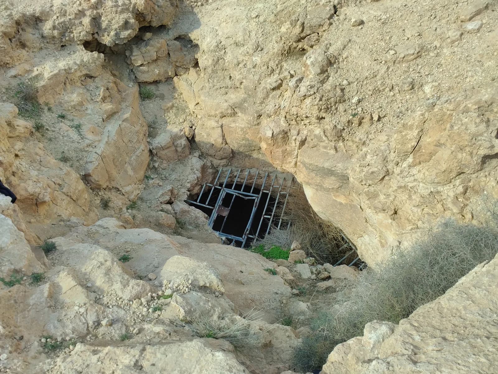 הפתח האנכי של מערת אשלים בתחתית שקע סלעי, ובו סורג מתכת