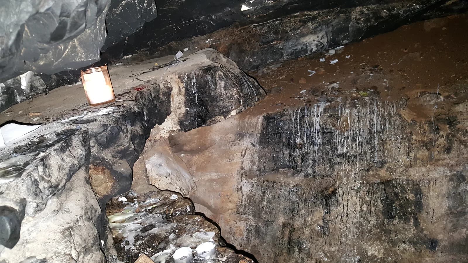 בתוך המערה: דופן סלע מושחרת מעשן נרות ונר דולק שהניחו מבקרים