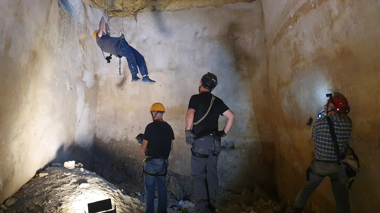 צוות סיור בתוך אחד מבורות המים החצובים והמטויחים במבצר ארטבה, ואחד המשתתפים גולש בחבל מפתח התקרה