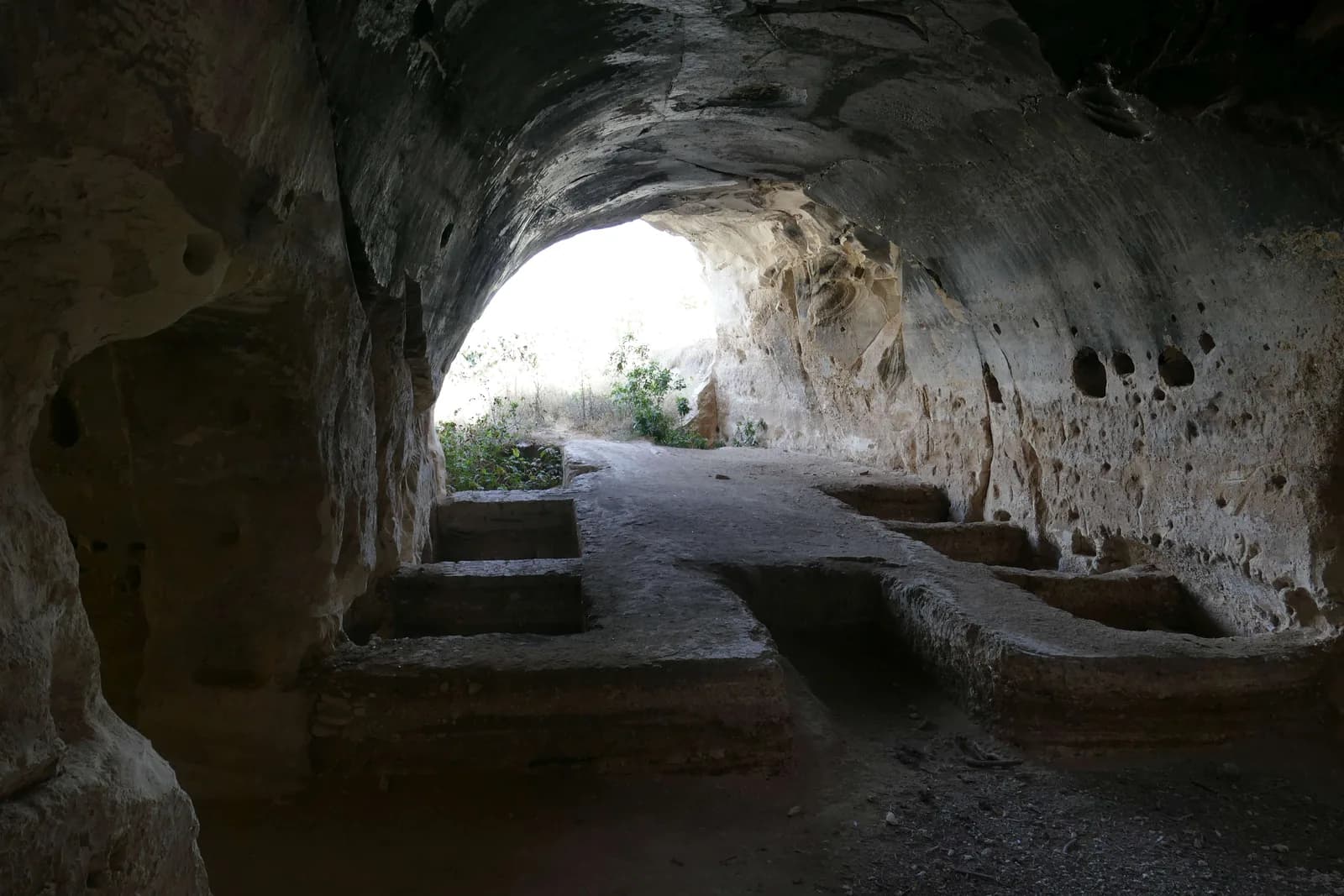 מעבר מקומר במערה ובו מתקנים מלבניים חצובים ברצפה, ופתח אור בקצהו