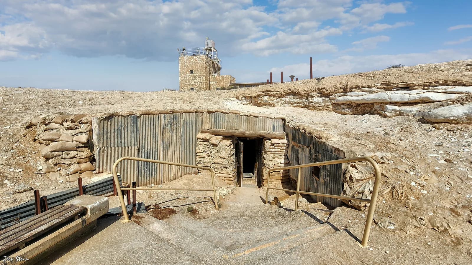 כניסה מבוצרת בשקי חול ופח גלי אל מערה תת-קרקעית במצפה, ומאחוריה המגדל