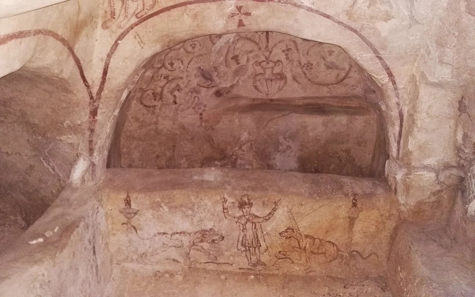 כוך קשת מצויר בשריגי גפן, צלב וציפורים, ומתחתיו סצנת דניאל בגוב האריות