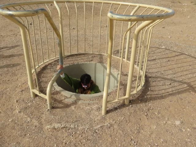 מטייל יורד לאחד הפירים המשוחזרים של בארות השרשרת, בתוך גדר המתכת
