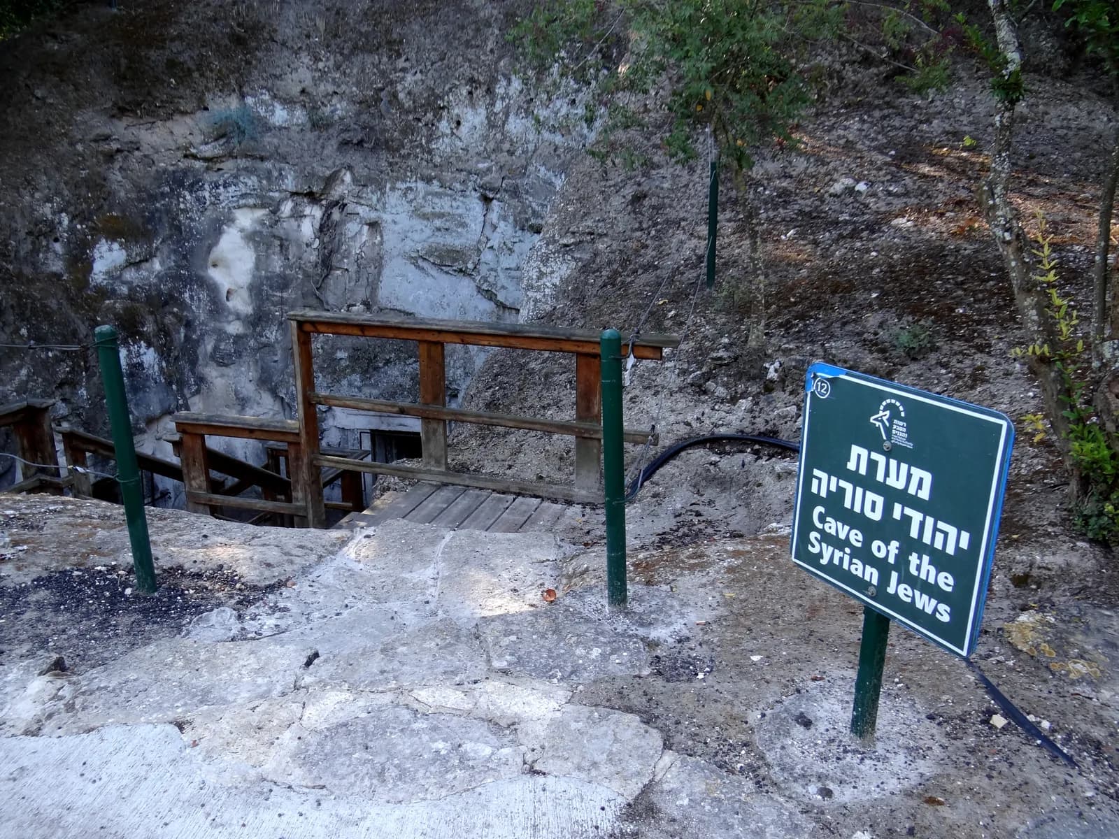 שלט מערת יהודי סוריה ומדרגות העץ היורדות אל חצר המערה