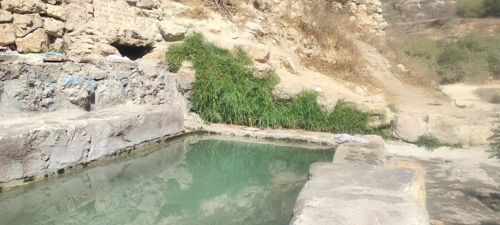 בריכת עין איתמר ומעליה פתח נקבת המעיין ולוח הזיכרון