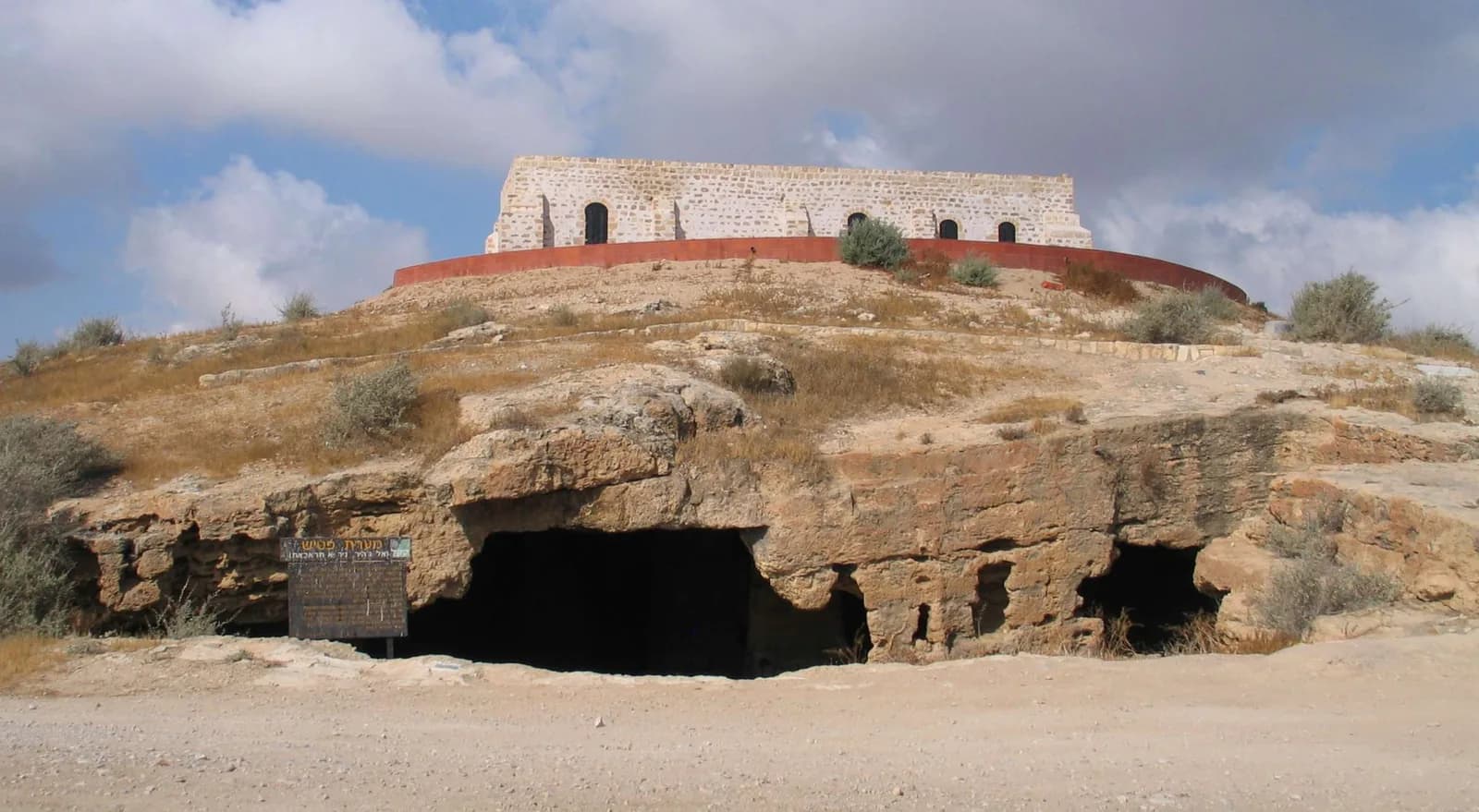 פתחי מערת פטיש בשיפולי הגבעה, ומעליה מצודת פטיש המשוחזרת