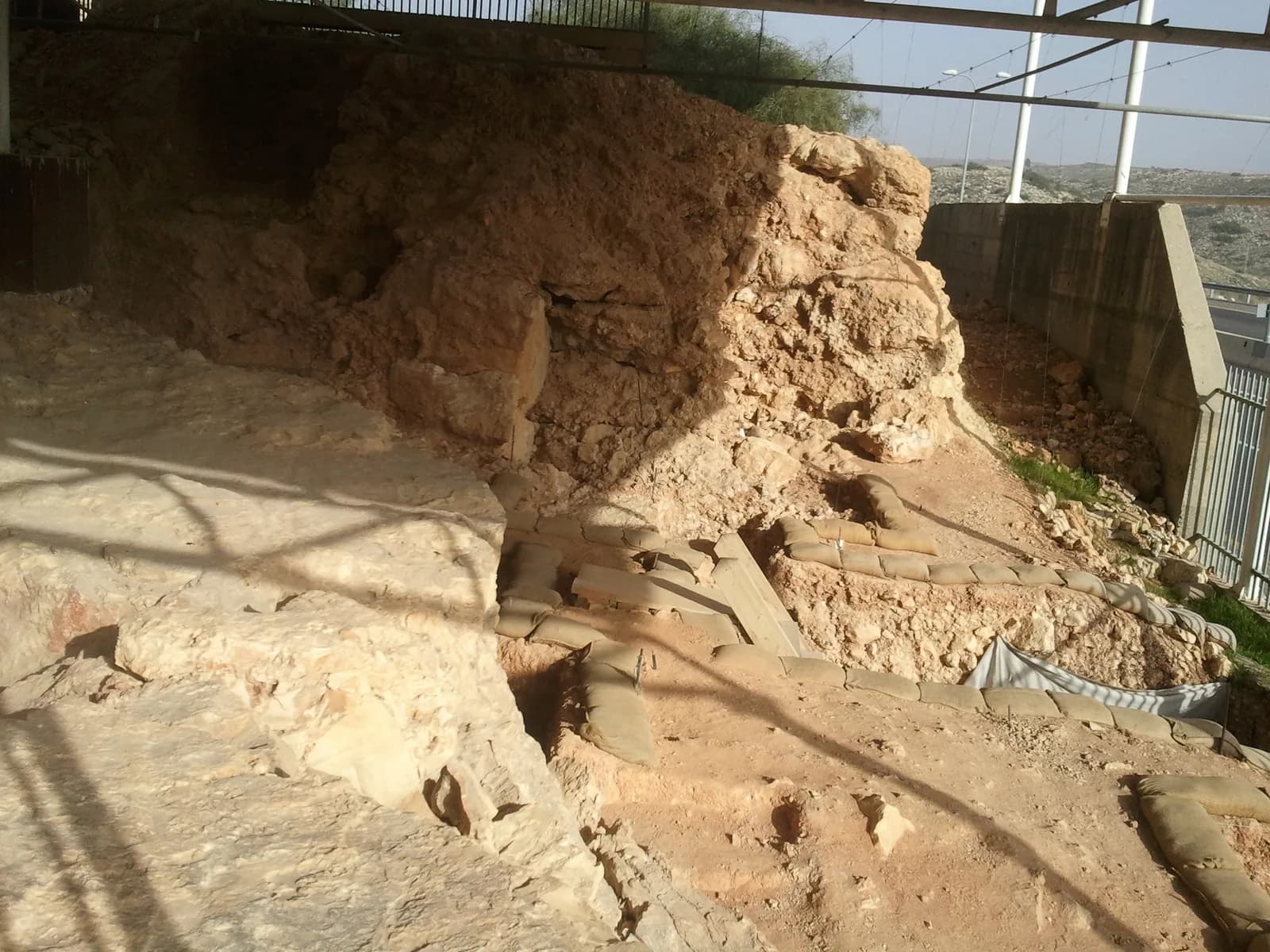 שרידי סלע המערה ושטחי החפירה המוגנים בשקי חול מתחת לגג המגן