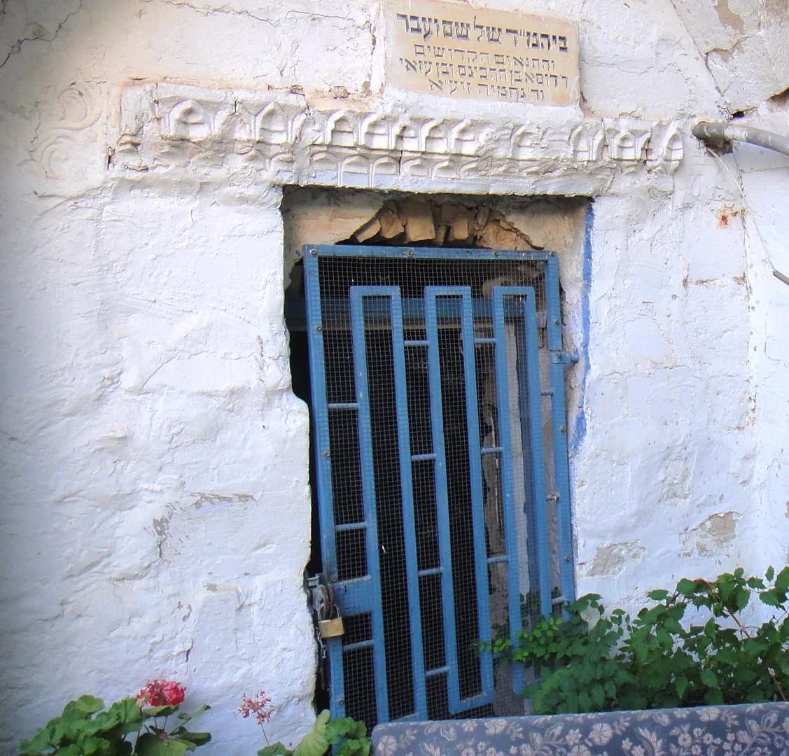 פתח המערה הסגור בסורג, ומעליו כתובת המזהה את המקום כבית המדרש של שם ועבר