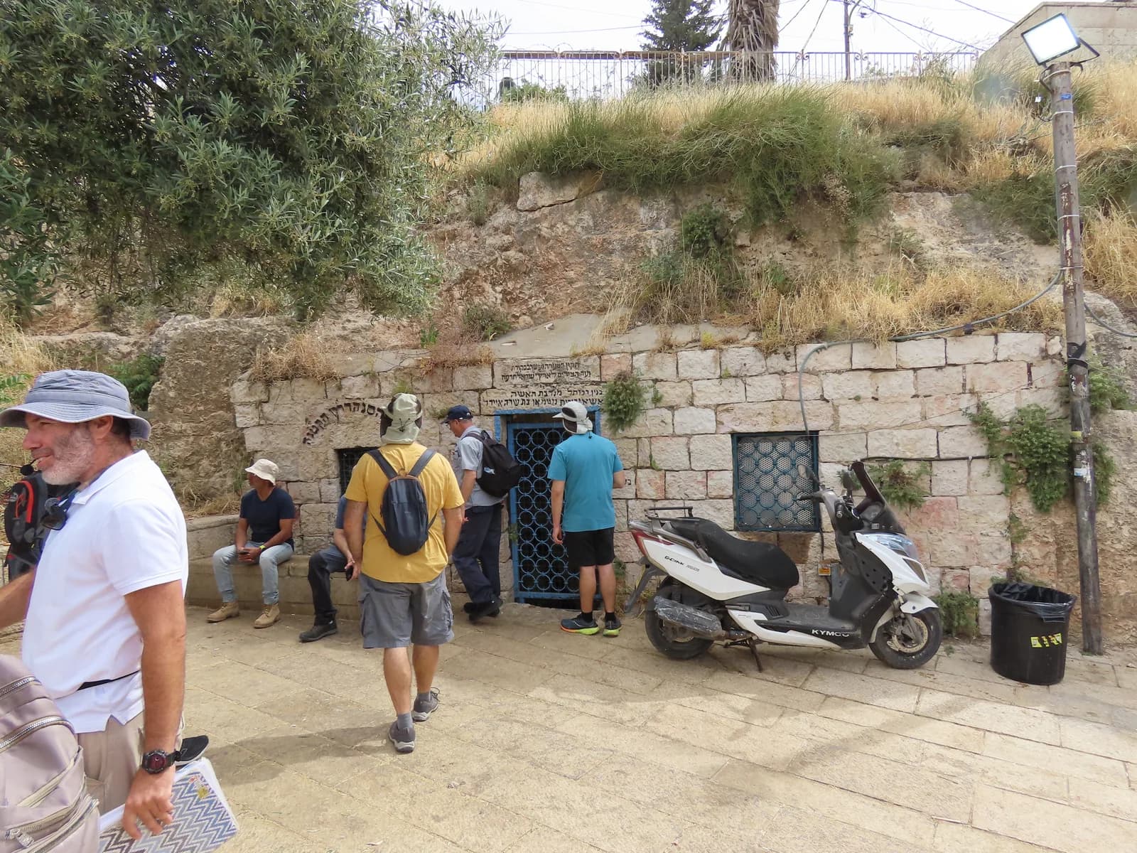 חזית המערה בשיפולי המדרון הסלעי, עם מבקרים ברחבה שלפניה