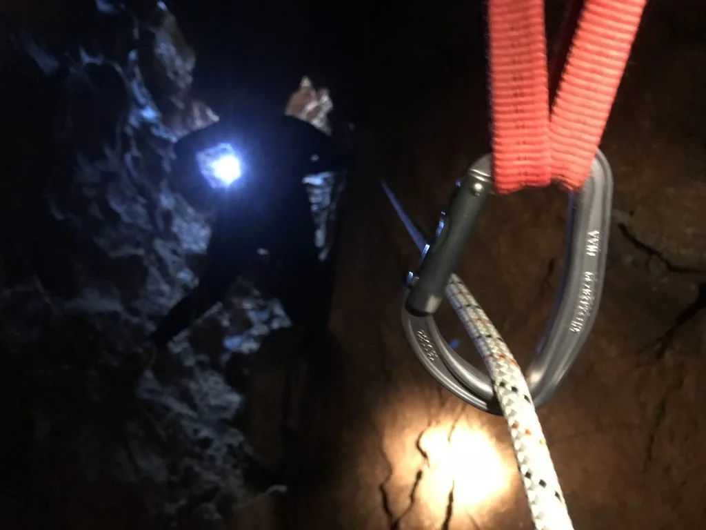 מערן עם פנס ראש וטבעת אבטחה על החבל בחשכת המערה