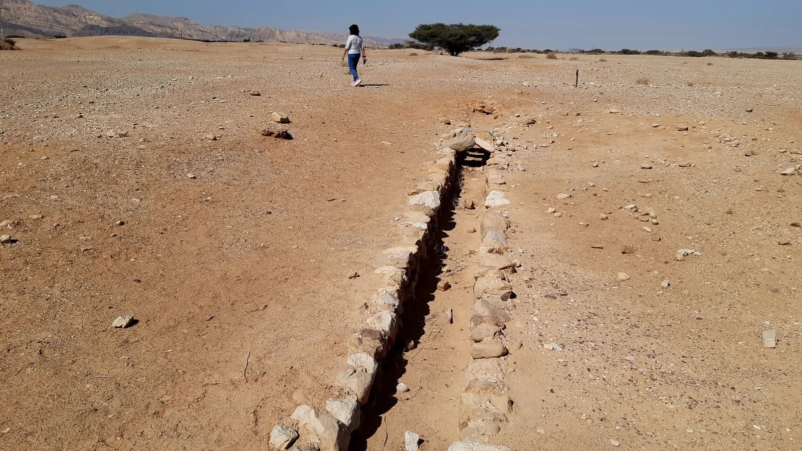 תעלת מים בנויה אבן בחוות עברונה, ובמרקע הרי אילת