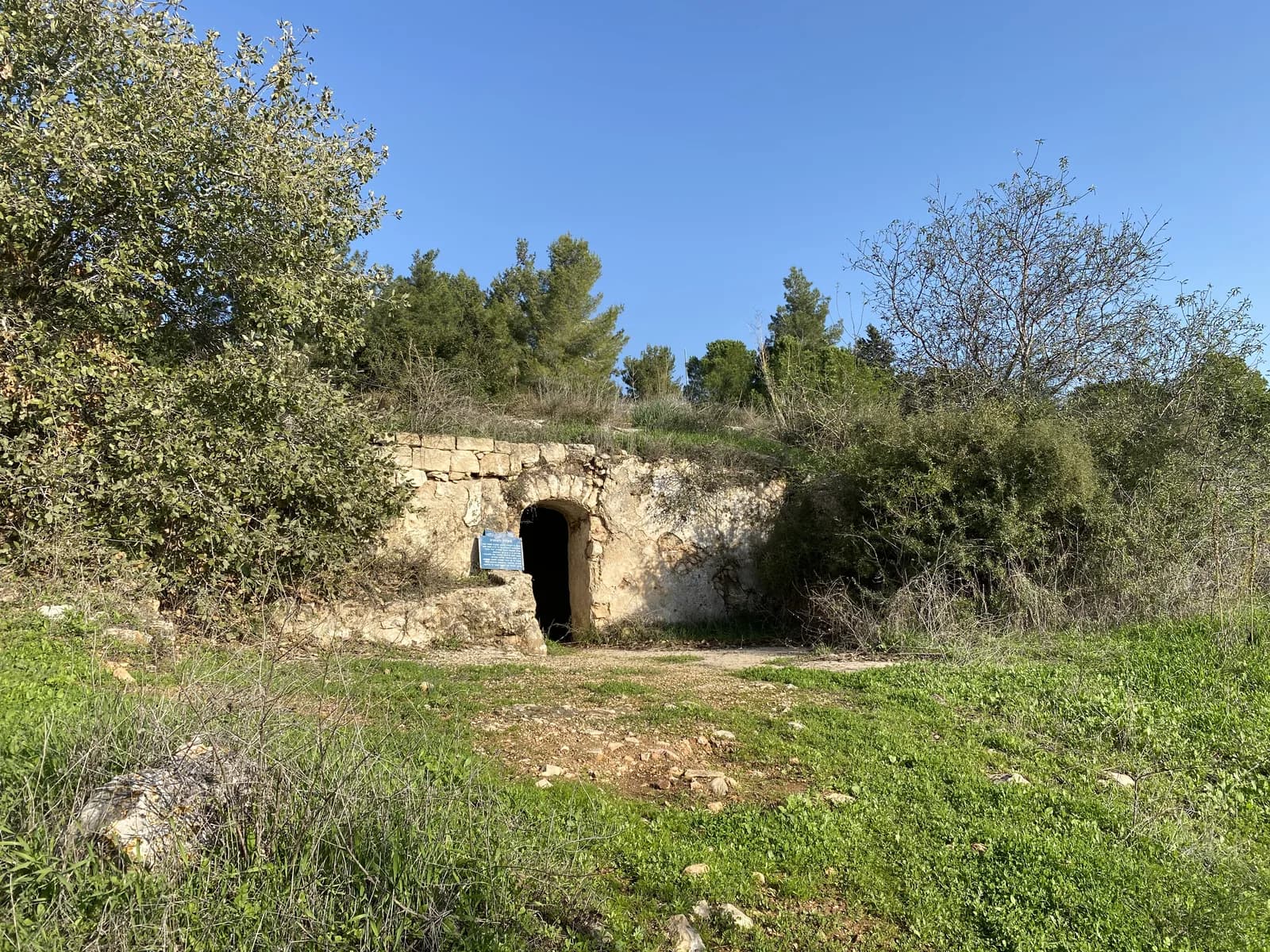 חזית האבן והפתח המקושת של מערת המקווה בסג'רה, ולצדו שלט ההסבר