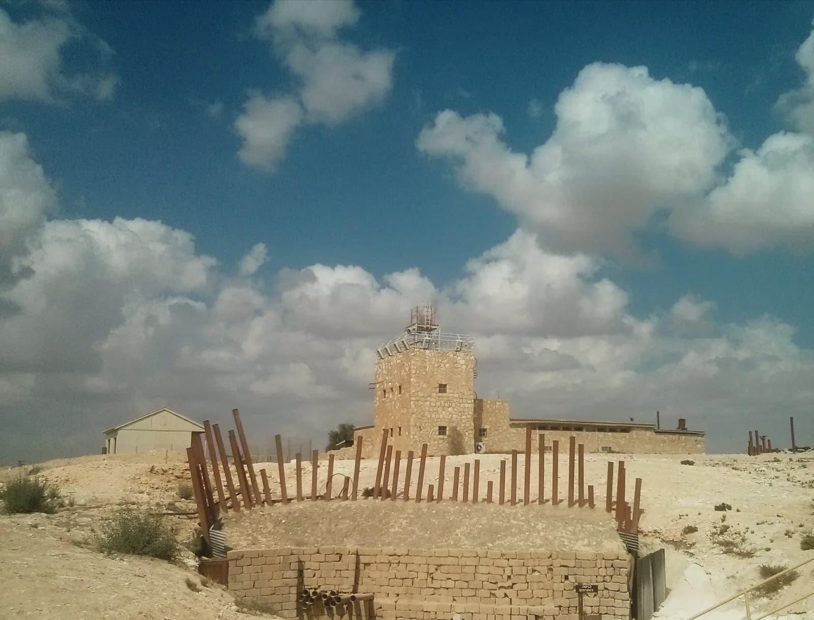 חזית המערה הגדולה עם צינורות הברזל שהפכו לסמל האתר, ומאחוריה מגדל מצפה רביבים