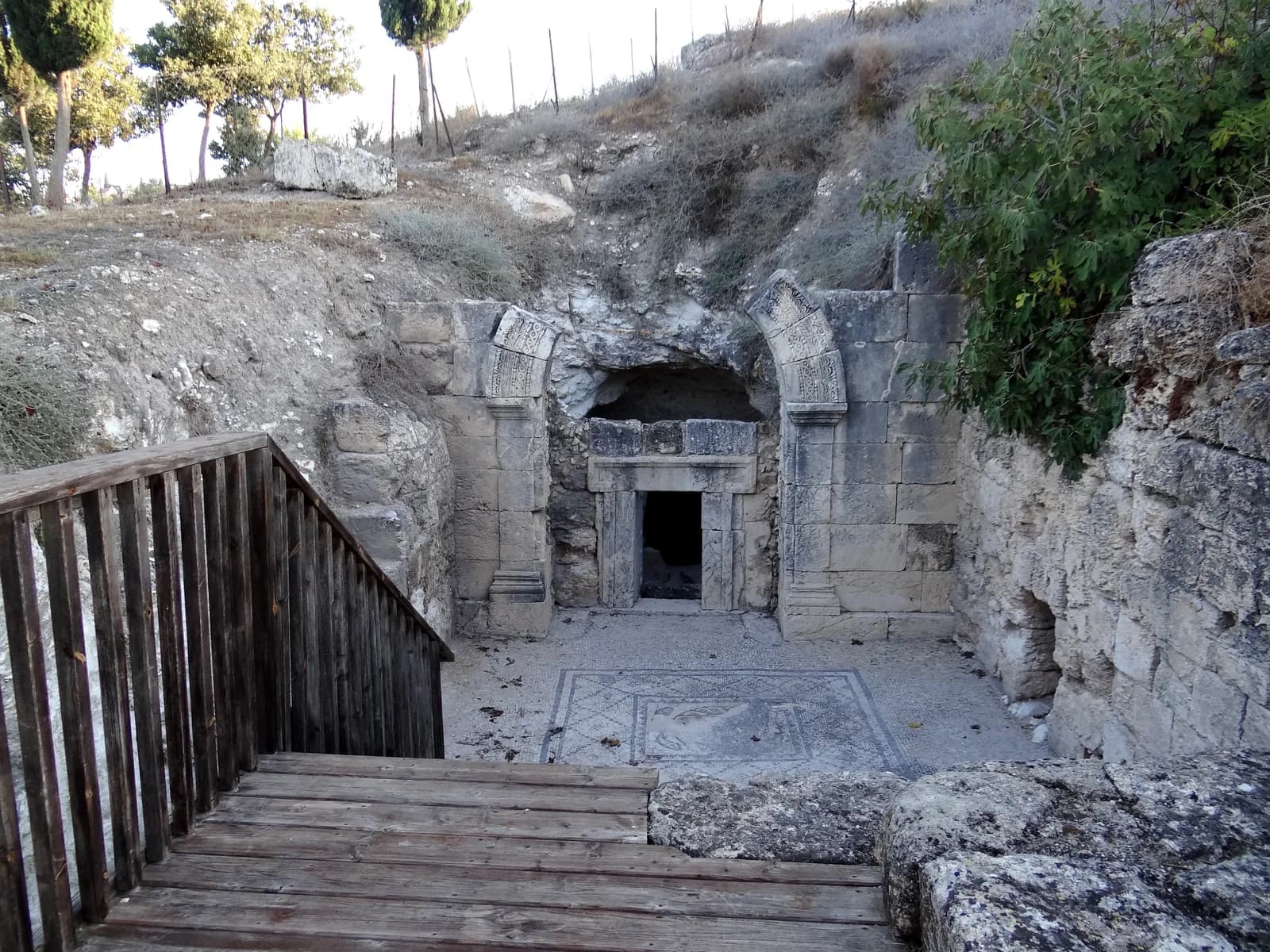 מדרגות העץ יורדות אל חצר מערת המאוזוליאום, אל רצפת הפסיפס והחזית הבנויה של מערה 11