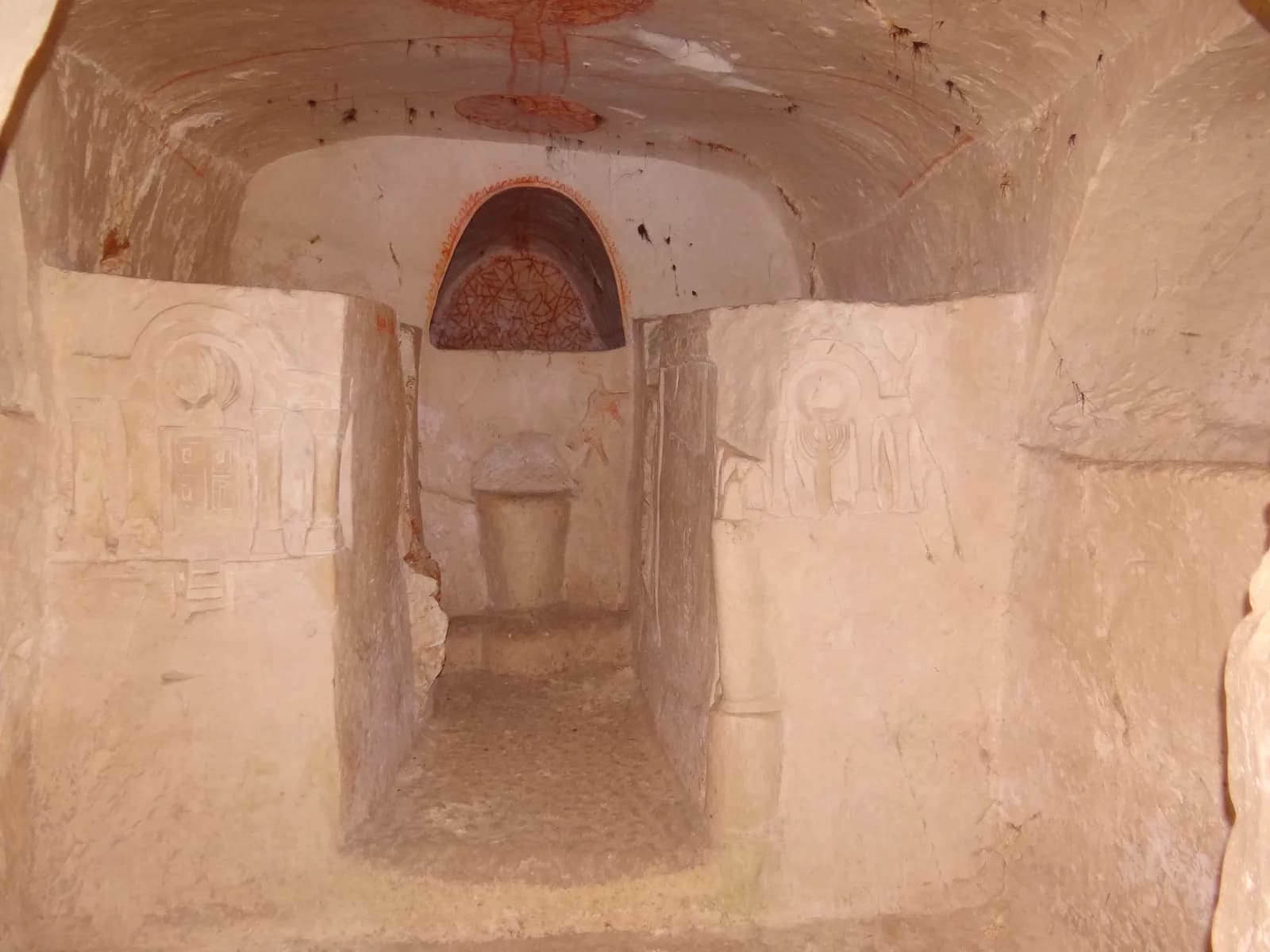 אולם במערת ארון הקודש: מעבר צר בין קירות חצובים ובהם תבליטים, ובקצהו קבר מקמר מעוטר בציורי אדום