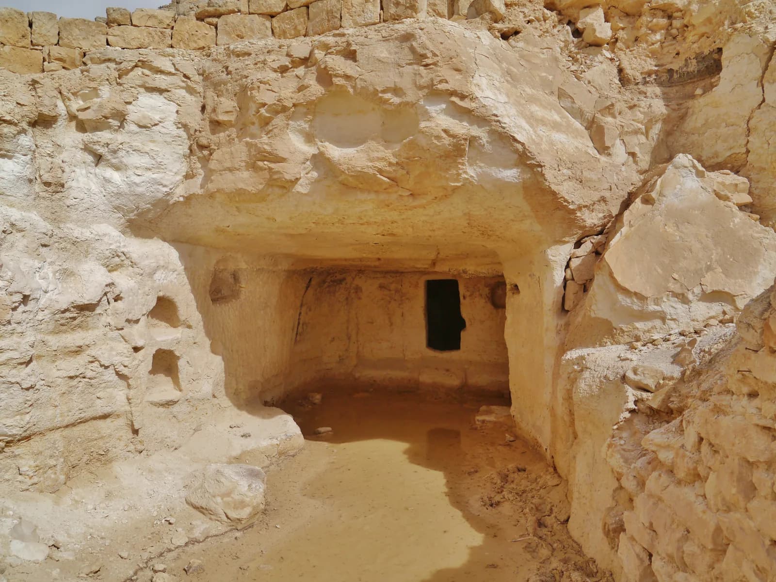 פתח מערה חצובה במדרון עבדת, ומעליה שרידי קירות בנויים